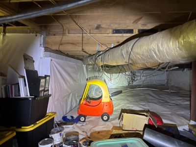 An active crawlspace encapsulation project with plastic sheeting being installed on walls and floor, plastic ductwork