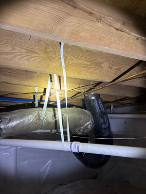 Interior crawlspace drainage system installation with white PVC pipes and black discharge line being positioned beneath
