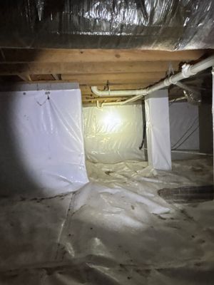 Active crawlspace encapsulation installation with white vapor barrier sheeting and interior drainage pipe visible along