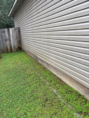 Exterior view of a metal-sided building foundation with an adjacent grassy area and wooden fence, showing no visible