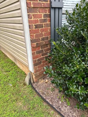 Exterior view of a residential foundation showing brick wall, siding, lawn, and landscaping with no visible repair work