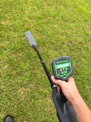 A technician uses a moisture meter to assess soil conditions on a lawn, likely measuring moisture levels during site