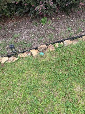 Exterior yard drainage system installation with a black perforated drain pipe laid along the lawn edge adjacent to