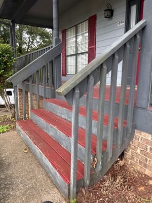 Exterior view of a residential house entrance with a covered porch, wooden railings, and brick foundation, showing no
