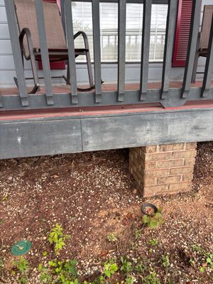 Exterior foundation view showing a mobile home or RV with metal skirting, brick pier supports, gravel ground with