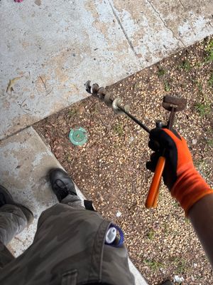 A worker in an orange safety glove is installing or adjusting exterior yard drainage pipe or channel along a concrete