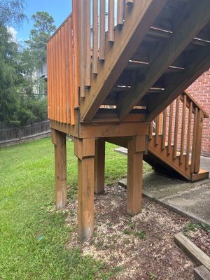 A wooden elevated deck or structure with support posts and undercarriage visible above a gravel base and green lawn,