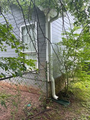 Exterior downspout and gutter system with visible drainage pipe routing water away from the foundation into the yard,