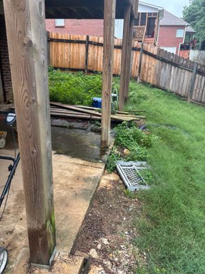 Exterior view of a house foundation with visible yard drainage infrastructure including a catch basin or drain box