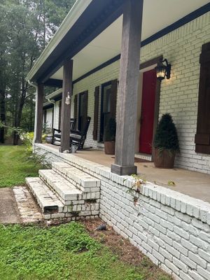 A residential home exterior with a covered porch, brick foundation, and manicured lawn showing no visible foundation