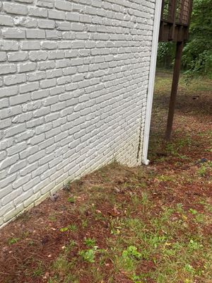 Exterior view of a white brick foundation wall with adjacent ground showing grass and soil, with no visible repair work