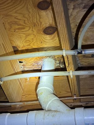 Interior crawlspace drainage pipe installation showing white PVC discharge line being routed through wooden framing and
