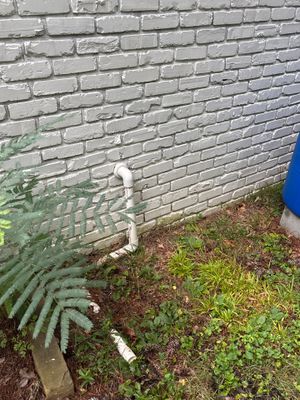 Exterior foundation area with white PVC drainage pipe installed along the brick wall base and yard-drainage components