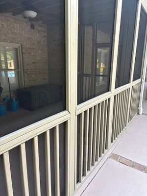 A screened porch or sunroom exterior showing a white-framed screen enclosure with brick foundation visible through the