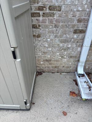 A narrow exterior foundation alcove or crawl space entrance showing a concrete floor with brick wall, no visible repair