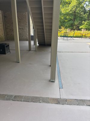 An interior foundation area under construction showing freshly poured concrete flatwork with a visible drainage channel