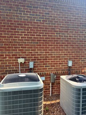 Two HVAC condenser units installed against a brick foundation wall with no visible foundation repair or waterproofing