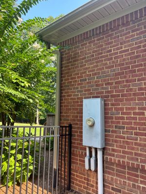 Exterior view of a brick house with landscaping and a metal gate, showing no visible foundation repair or waterproofing
