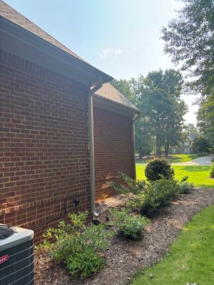 Exterior view of a brick foundation with landscaping and lawn, showing no visible repair work or drainage hardware