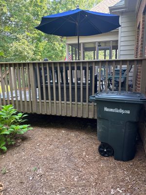 A residential deck with blue umbrella and trash bin visible, showing the exterior of a house with no visible foundation