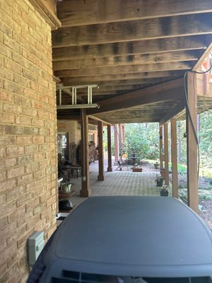 A covered porch or breezeway area with brick walls, wooden beams, and an open view to the yard, showing no visible