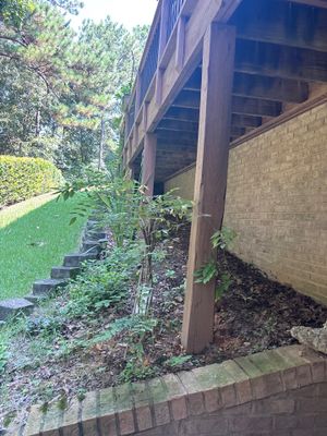 Exterior view of a house foundation with brick veneer, a covered structure, and landscaping showing the pre-work