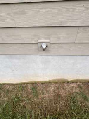 Exterior view of a house foundation showing the transition between siding and concrete with grass and soil at ground