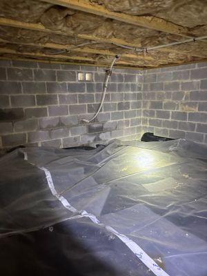 A crawlspace undergoing encapsulation work with a plastic vapor barrier being installed on the floor and drainage