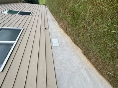 Completed exterior drainage installation showing a concrete pad adjacent to a composite deck with a drainage outlet and