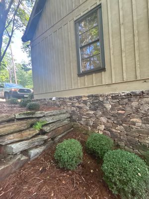 Exterior view of a stone foundation with landscaping showing healthy shrubs and mulch, with no visible repair work,