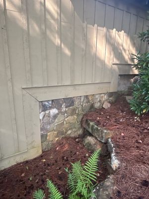 Exterior foundation area with a metal drainage channel installed against the concrete foundation wall, surrounded by