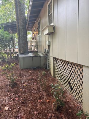 Exterior foundation perimeter showing mulched ground, lattice skirting, and a gray drainage box or catch basin visible
