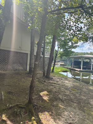 Exterior view of a mobile home or RV on blocks near a waterway with mature trees, showing the site before any