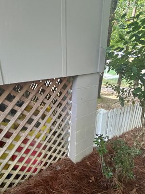 An exterior foundation area showing a lattice trellis installed against the house foundation with mulch and landscaping