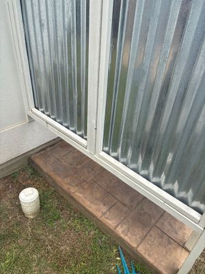 Exterior foundation view showing a brick foundation wall with a white PVC downspout and blue drainage line on the