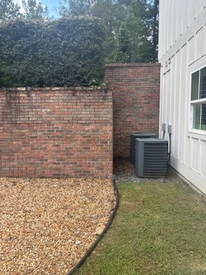 A side yard view of a white house with brick foundation walls, gravel and grass landscaping, and an HVAC unit, showing