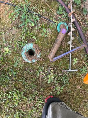 Exterior yard drainage installation in progress showing excavated drain pipes with blue connectors and a catch basin