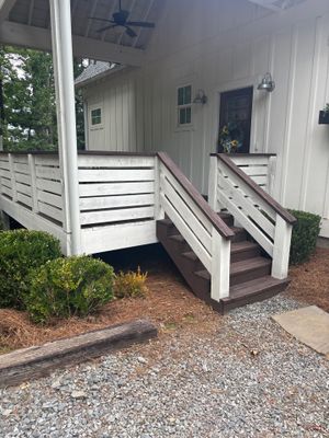 Completed exterior foundation work showing a raised deck/porch with new white railings, gravel yard drainage, and