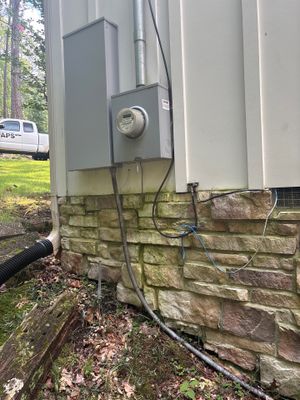 Exterior foundation area showing installed black drainage pipe running along the base of a house with stone foundation,