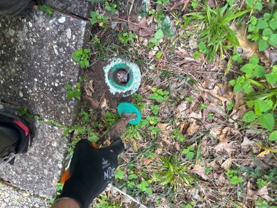 An exterior catch basin or drain box with turquoise/teal coloring is visible in a grassy yard area during installation,