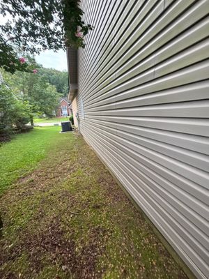 Exterior view of a residential home's side with metal siding, showing the foundation area, lawn, and landscaping with