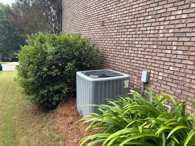 Exterior view of a brick foundation with an HVAC unit, landscaping, and lawn showing no visible repair work or drainage
