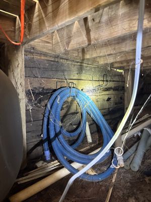 Interior crawlspace or basement showing blue drainage pipe coiled and staged, with wooden framing and foundation