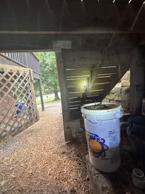 Exterior crawlspace or foundation area with a blue drain bucket/catch basin and gravel surface during yard drainage