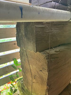 A wooden fence or deck structure showing weathered, discolored wood with visible decay and moisture damage at the post