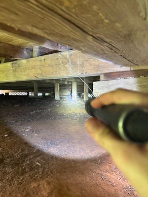 Crawlspace under a structure showing interior drainage piping and preparation work in progress, with wooden beams