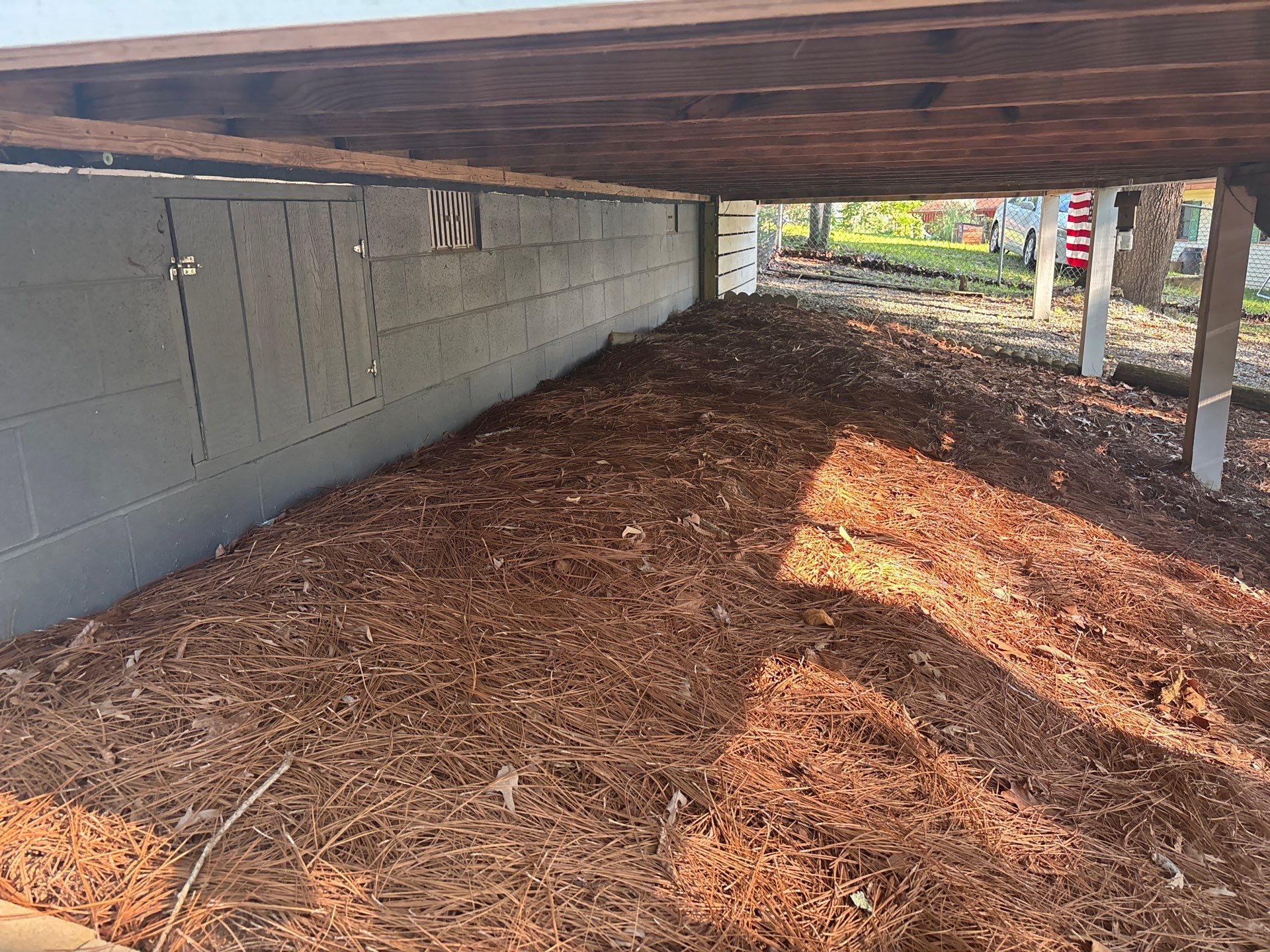 An exterior covered structure or carport with a concrete foundation wall and mulched ground surface, showing the