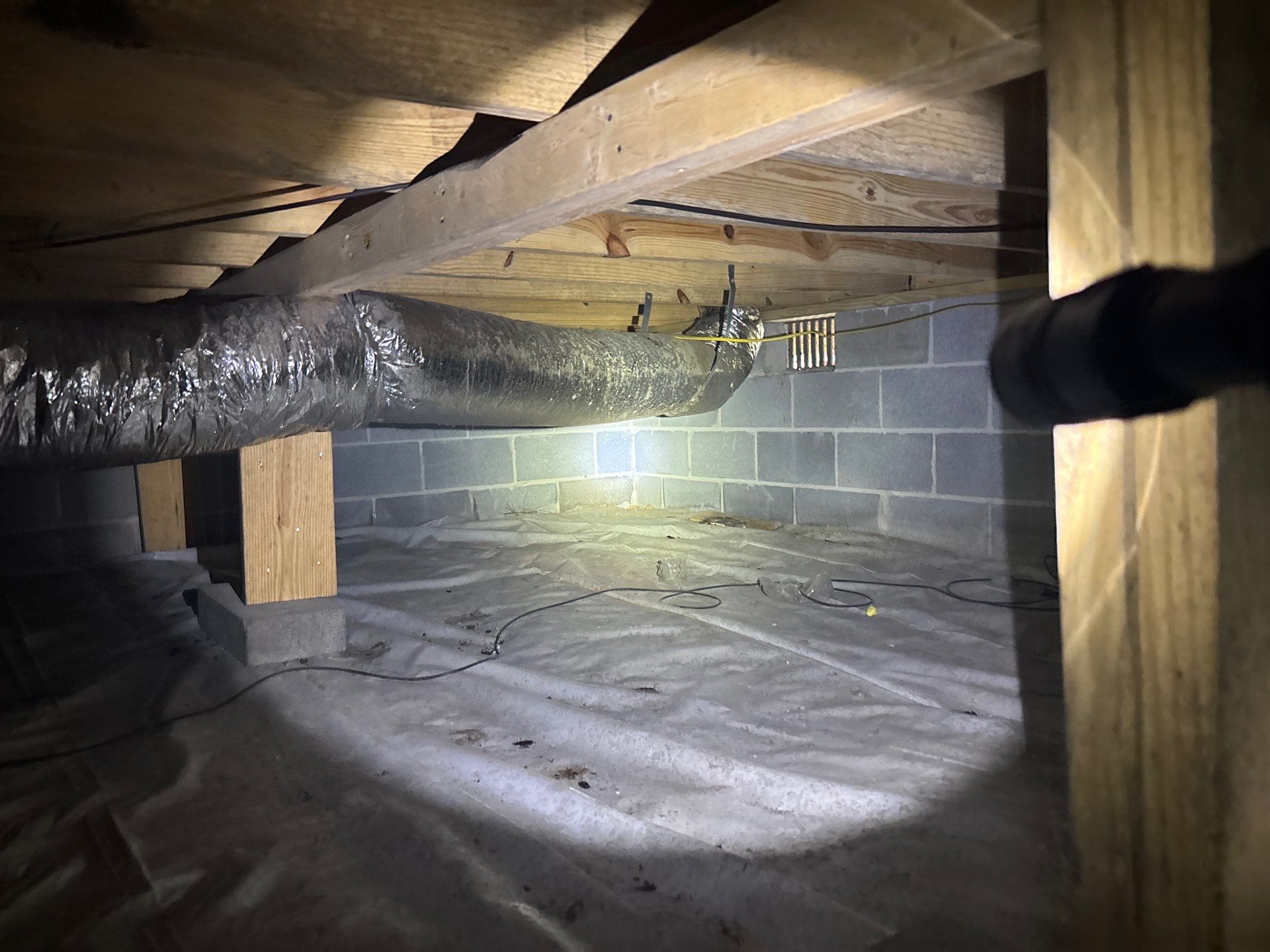 An active crawlspace encapsulation and drainage installation in progress, showing a vapor barrier being installed,