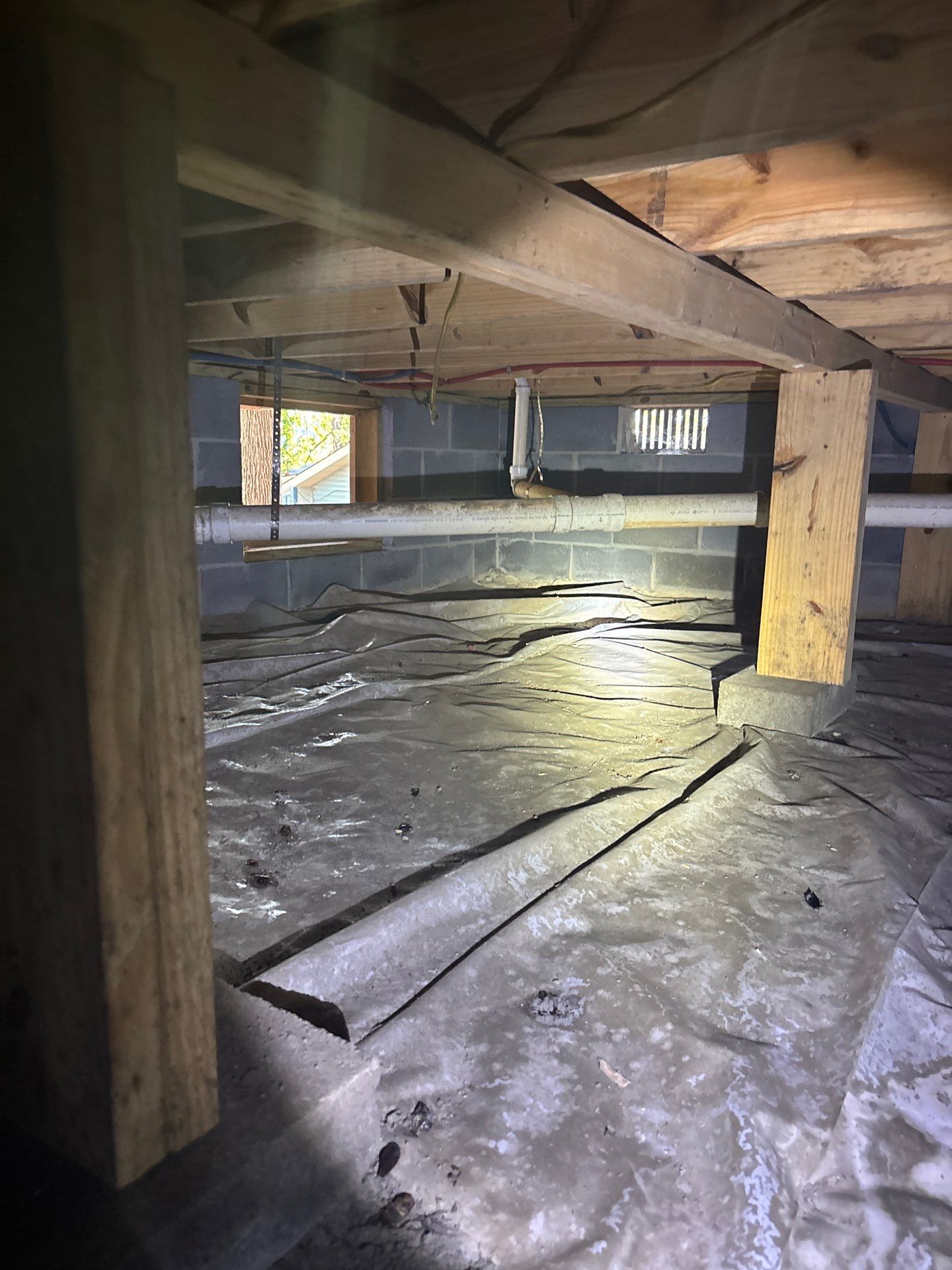 Active crawlspace encapsulation and drainage work in progress, showing vapor barrier installation, support posts, and