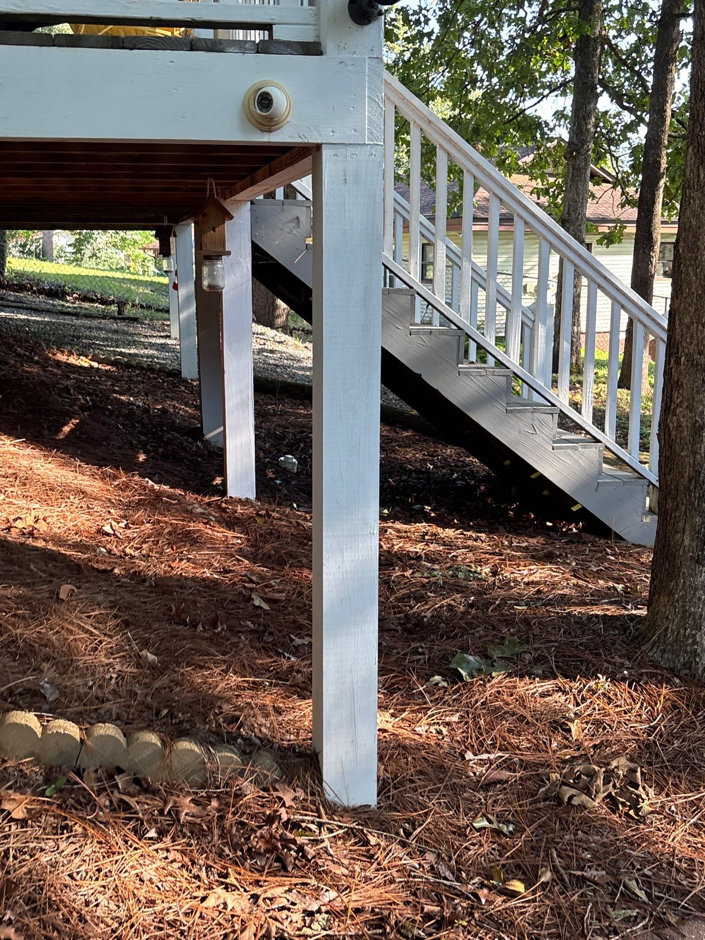 Completed exterior foundation work showing a white support post, deck stairs with railing, and graded yard drainage